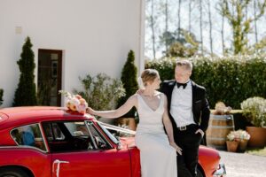 A Tuscan inspired wedding in Christchurch bride and groom in front of a villa with a red classic car