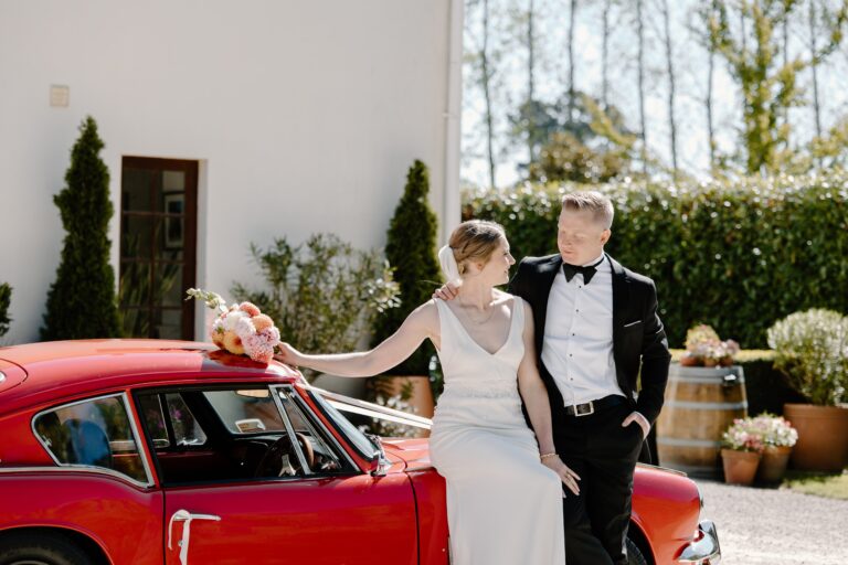 A Tuscan inspired wedding in Christchurch bride and groom in front of a villa with a red classic car