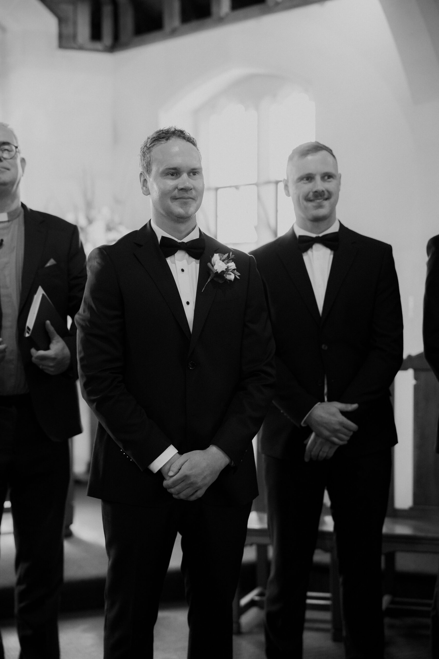 Black and White photo of the groom standing at the top of the aisle before the wedding ceremony in a church