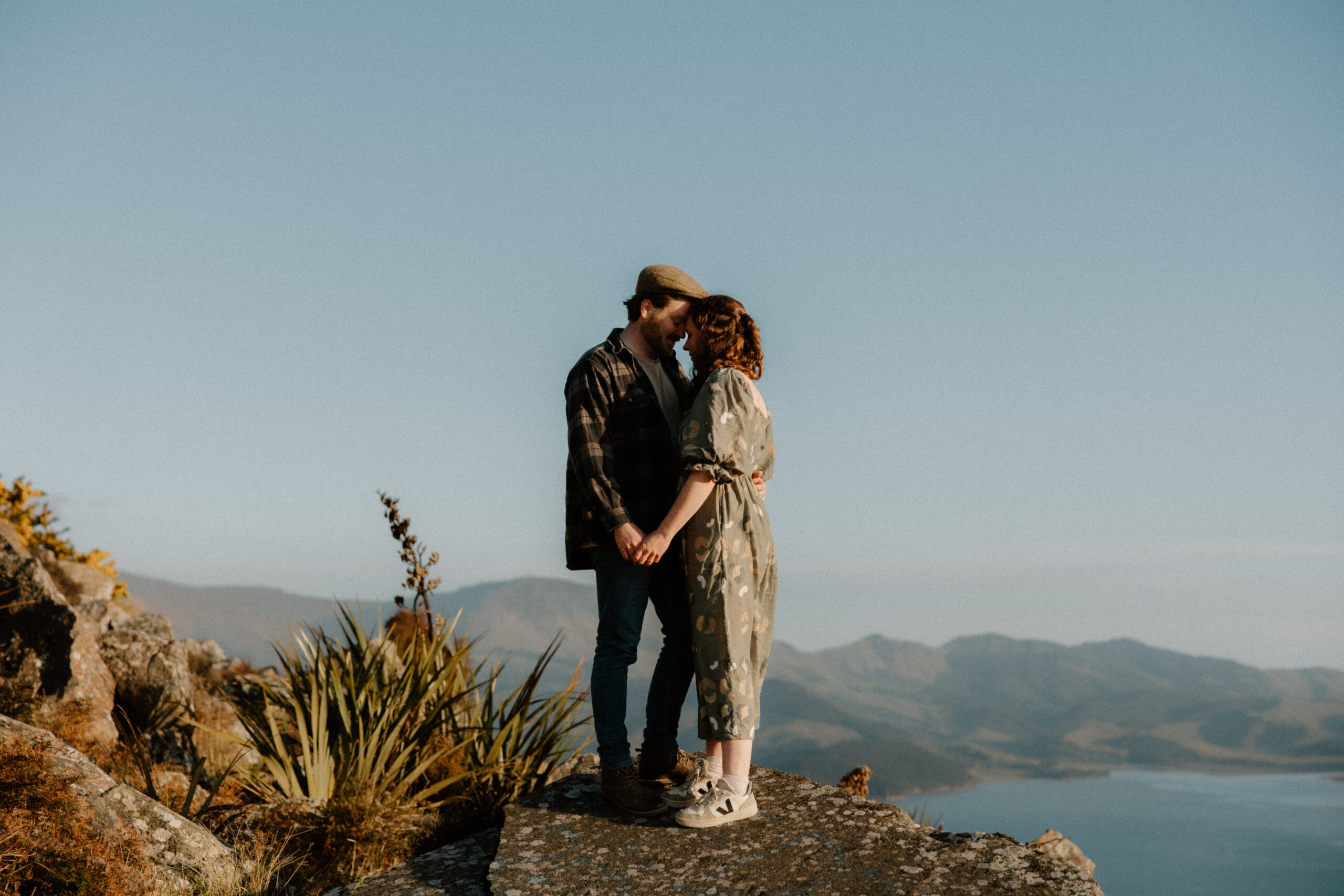 Couple holding hands overlooking Lyttleton Harbour during an engagement session at Rapaki Rock in the Port Hills, Christchurch.