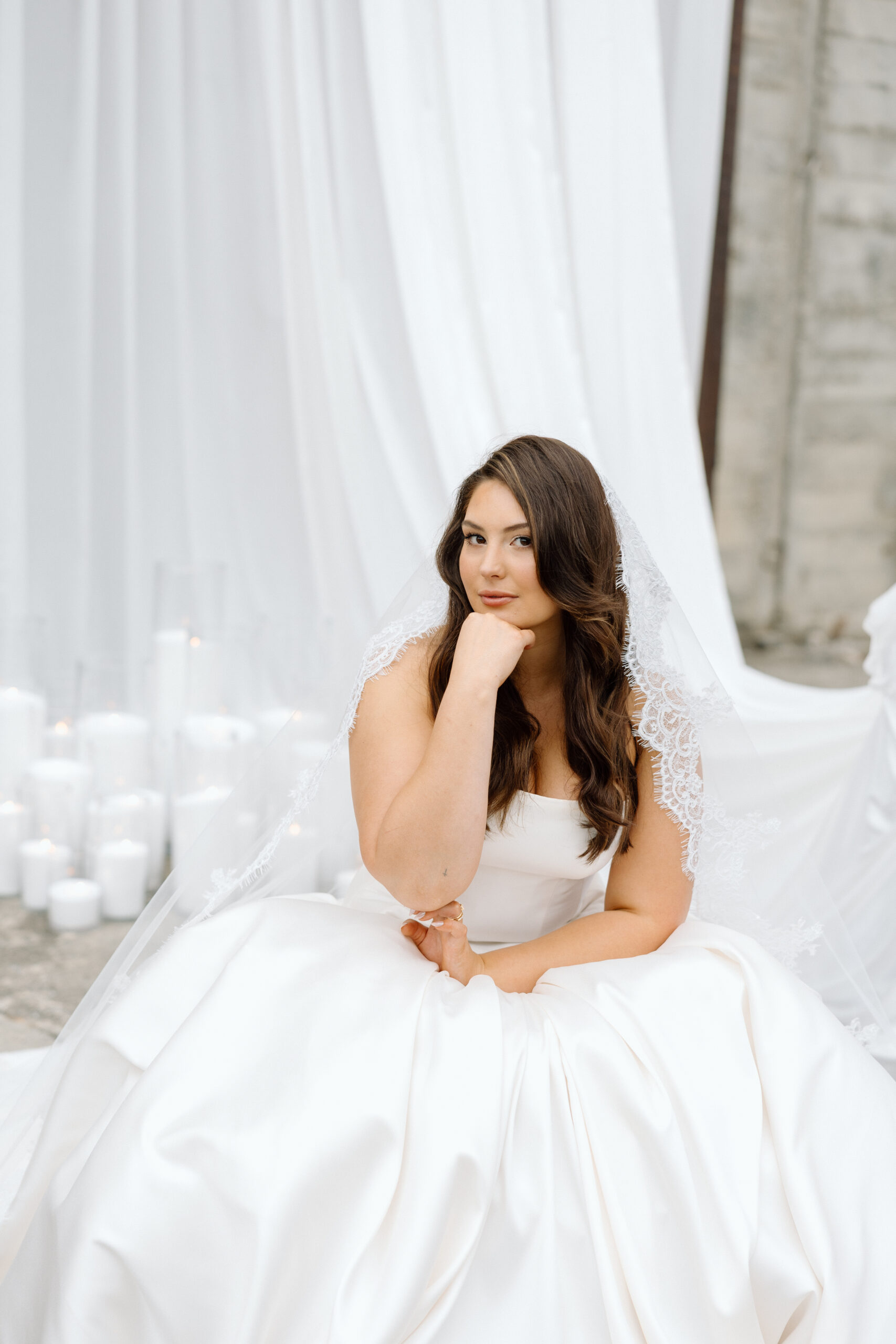 Bride in a strapless satin corset gown with a drop-waist skirt standing behind a styled wedding table, beneath a white ruffled umbrella at The Flaxmill in Oxford, New Zealand